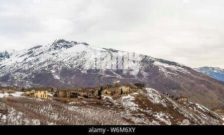 Telaio di panorama di montagna innevata con alberi sfrondato multipiano case e visualizzati su strada in inverno Foto Stock