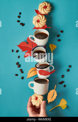 Tempo autunnale, torre di bilanciamento di tazze da caffè, foglie di autunno e notebook su sfondo blu Foto Stock