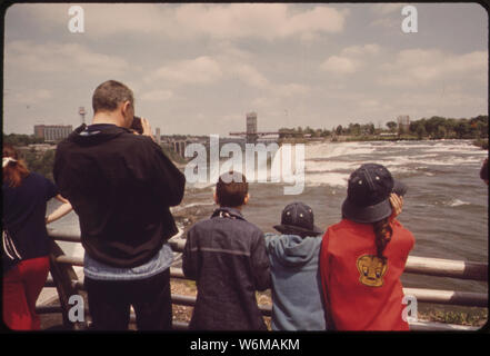 I turisti sul Ponte di Arcobaleno che attraversa il fiume Niagara appena sotto le cascate. Le cascate Americane e torre di osservazione sono sulla destra. IN BACKGROUND sul lato Canadese è il SKYLON torre di osservazione Foto Stock