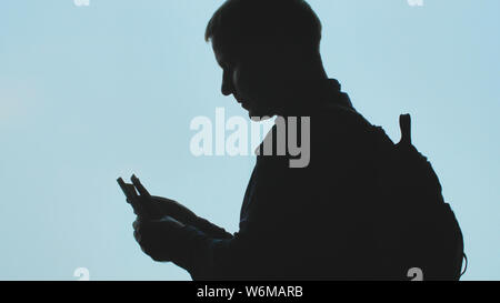 Silhouette di un giovane uomo contando di dollari contro il cielo blu. Foto Stock