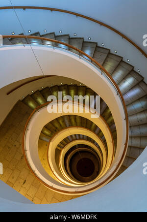 Scala a spirale conduce giù diversi piani con illuminazione drammatica. Foto Stock