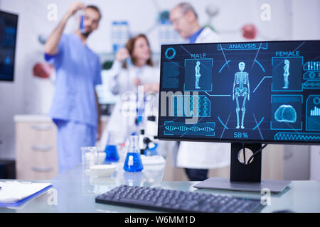 Display monitor in un laboratorio ospedaliero che mostra scheletro umano. Team di scienziato che lavora in background. Foto Stock