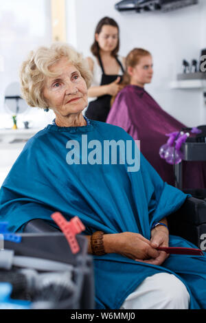 Eleganti Donna senior per parrucchieri capo seduto nella sedia del barbiere, attesa per il taglio dei capelli Foto Stock