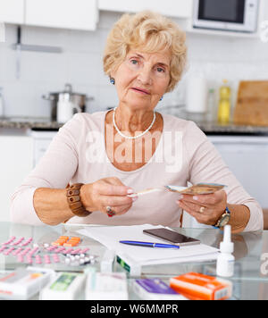 Senior donna contando la sua spesa per pillole seduta in cucina Foto Stock