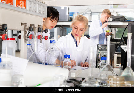 Due ragazze gli studenti della Facoltà di Chimica di eseguire esperimenti in laboratorio universitario, risultati di registrazione nella cartella di lavoro Foto Stock