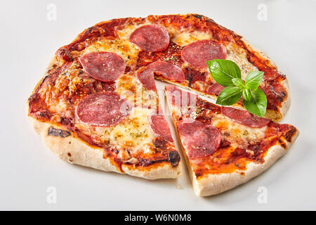 Fette di salame pizza guarnita con basilico fresco su uno sfondo bianco per la pubblicità o un menu Foto Stock