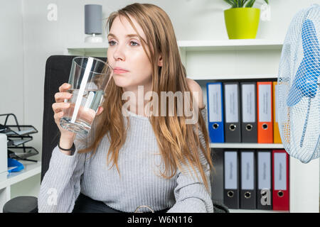 Una giovane donna viene sbalzato fuori calore in ufficio e di bere un po' d'acqua Foto Stock