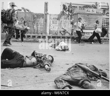 Con timore e inquietudine che mostra sulle loro facce e alla spinta del Sud soldati vietnamiti, donne e bambini caricato verso il basso con recuperati beni scurry passato i corpi dei tre Viet Cong uccisi in combattimenti., 05/1968; Note Generali: Utilizzo di guerra e di conflitto numero 423 quando si ordina una riproduzione o la richiesta di informazioni su questa immagine. Foto Stock