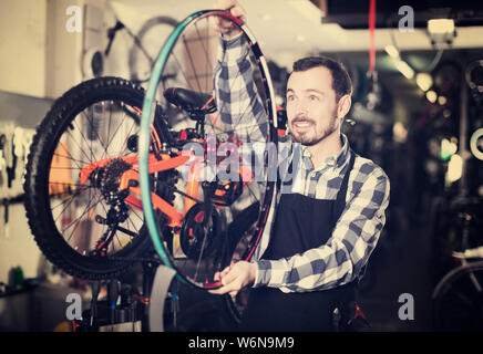 Uomo in grembiule mostra la struttura della ruota di bicicletta per articoli sportivi shop Foto Stock