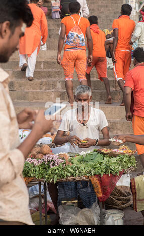 Un uomo indiano che vendono fiori per le offerte di puja mentre un uomo con uno smartphone è in primo piano Foto Stock