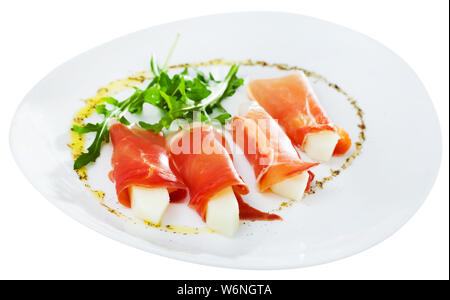 Lo spagnolo gustoso piatto di rotoli di prosciutto di Parma e melone servito con foglie di rucola in corrispondenza della piastra, vicino. Isolato su sfondo bianco Foto Stock