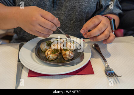 Mano umana utilizzando piccola forcella mangiando Escargots de Bourgogne Foto Stock