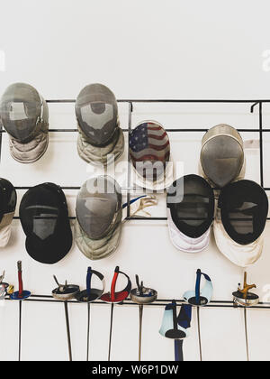 Gruppo di maschere di scherma e spada appesi al muro. Foto Stock