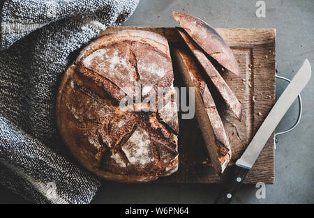 Flat-lay di pane appena sfornato pane di pasta acida pane e fette di pane rustico di legno su cemento grigio sfondo tabella, vista dall'alto Foto Stock