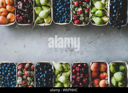 Estate frutta e bacche di varietà. Flat-lay di fragole mature, ciliegie, uva, mirtilli, pere, albicocche, fichi in legno eco-friendly scatole su Foto Stock