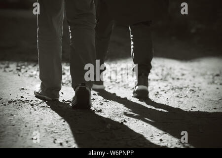 Immagine in bianco e nero del, dove i suoi piedi due uomo vestito di sneakers e pantaloni, andare a piedi sulla sabbia-rocky road. La gente va da leggero a darkne Foto Stock