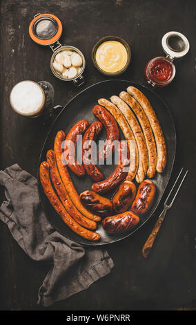 Piatto di laici Oktoberfest cena tabella concetto con grigliate di carne di vitello e di carne di maiale salsicce, salsa, decapati vaggies e birra in bicchieri su backgroun scuro Foto Stock