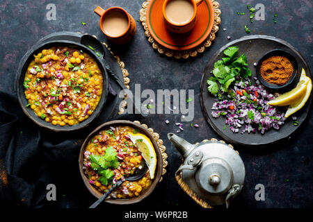 Indian vegan curry di lenticchie servita con un trito di cipolla, peperoncini verdi, il coriandolo fresco , le spezie e appena sfornati chai. Foto Stock