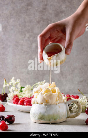 In casa di ricotta gelato alla vaniglia gelato servito in tazza ceramica con lamponi freschi, ciliegia bacche, elderflowers. Man mano sciroppo di colata dalla brocca. Foto Stock