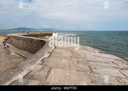 Guardando verso il fine di Cobb, Lyme Regis e il suo porto artificiale e le difese del mare: la gente camminare lungo la passerella superiore / a piedi modo. Regno Unito. (110) Foto Stock