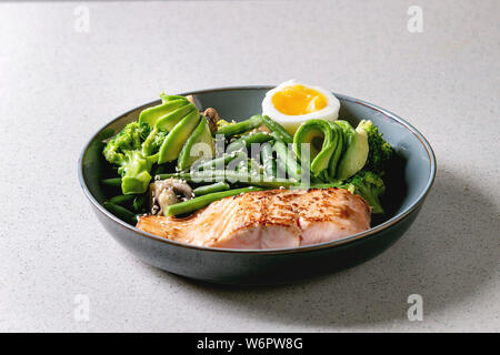 Ketogenic low carb la dieta a cena il salmone grigliato, avocado, broccoli, verde fagiolo e uova sode nel recipiente di ceramica sulla tabella grigia. Spazio di copia Foto Stock