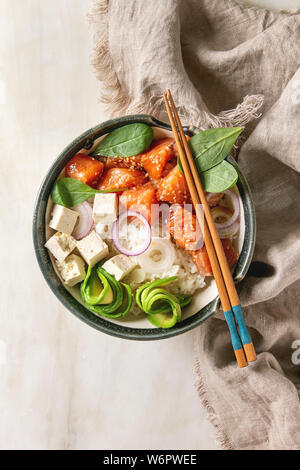 Poke ciotola con la salsa di soia salmone marinato, riso, avocado e tofu formaggio servita in tazza ceramica con bacchette su marmo bianco dello sfondo con la linea Foto Stock