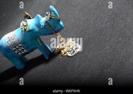 Gioielli su little blue rhino statua tenere il titolare di gioielli collana blu anelli oro blu e oro anelli con sfondo grigio piuttosto animale Foto Stock