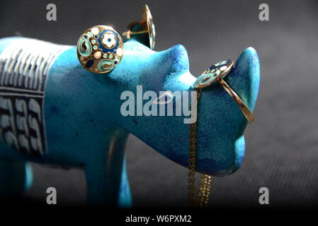 Gioielli su little blue rhino statua tenere il titolare di gioielli collana blu anelli oro blu e oro anelli con sfondo grigio piuttosto animale Foto Stock