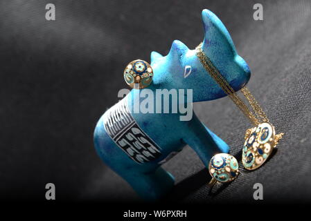 Gioielli su little blue rhino statua tenere il titolare di gioielli collana blu anelli oro blu e oro anelli con sfondo grigio piuttosto animale Foto Stock