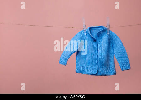 Carino lavorati a maglia new born baby jumper appeso su una linea di abbigliamento contro rosa Foto Stock