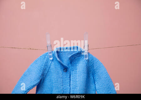 Carino lavorati a maglia new born baby jumper appeso su una linea di abbigliamento contro rosa Foto Stock