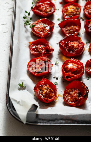 Arrosto di pomodori ciliegini, cosparsi di foglie di timo, sale marino e pepe nero pestato, su un forno vassoio. Foto Stock