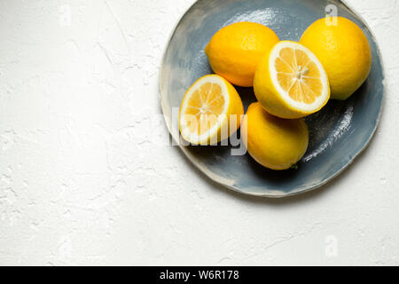 Limoni freschi interi e tagliate a metà, disposti su una mano blu piastra realizzata. Foto Stock