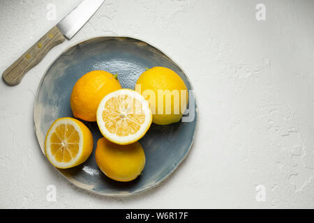 Limoni freschi interi e tagliate a metà, disposti su una mano blu piastra realizzata. Un di legno trattate coltello è accanto a. Foto Stock