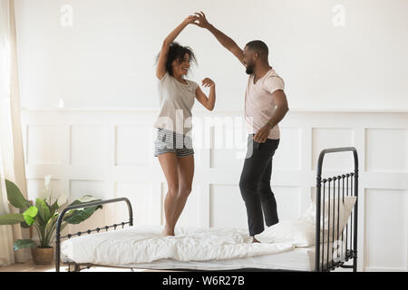 Giovane romantico americano africano giovane indossando pigiami ballando sul letto Foto Stock