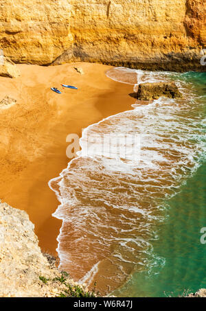 Due stand up paddling commissioni a sinistra dietro alla spiaggia in una bellissima insenatura abbandonati con vibrante di sabbia arancione e verde acqua (ritratto verticale orient Foto Stock