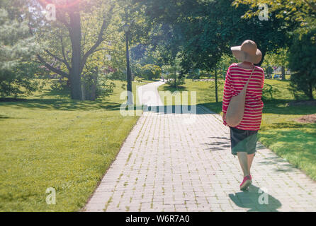 Signora a piedi attraverso il parco, visto da dietro. Foto Stock