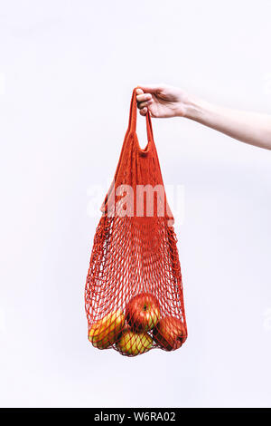 Mano femmina trattiene un cotone rosso shopping bag con arance e mele Foto Stock