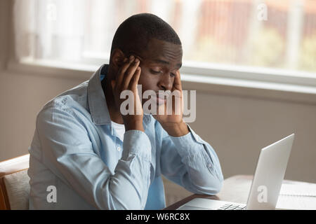 African ragazzo seduto vicino al computer lo sfregamento dei templi si sente male Foto Stock