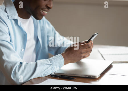 Ritagliato closeup immagine ragazzo africano sedersi a tavola utilizza lo smartphone Foto Stock