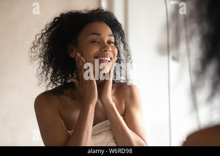Donna africana dopo la doccia guardare in mirror di toccare la pelle delicata Foto Stock