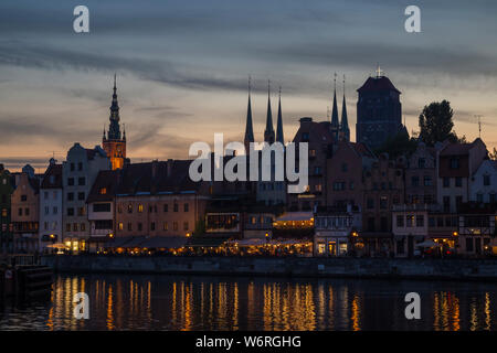 Vista panoramica di lit campanili e altri edifici antichi lungo il ponte lungo waterfront presso le principali città della Gdansk, Polonia, in prima serata. Foto Stock