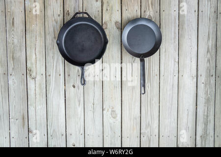 Tradizionale vs nuovo pentole battaglia - ghisa versus acciaio al carbonio o in teflon. Sfondo di legno. Più sano utensile di cottura opzioni. Vuoto testo vuoto r Foto Stock