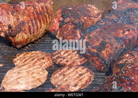 Punta di petto di manzo e hamburger cottura di fianco a fianco su un open barbecue.la tradizionale fiera di strada cibo. Foto Stock