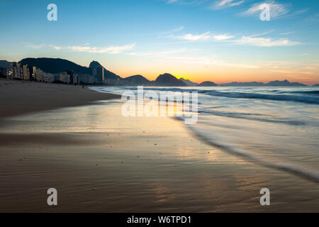 La mattina presto sulla spiaggia di Copacabana a Rio de Janeiro con lo Sugarloaf mountain in background prima del sorgere del sole con profondo arancione e blu Foto Stock