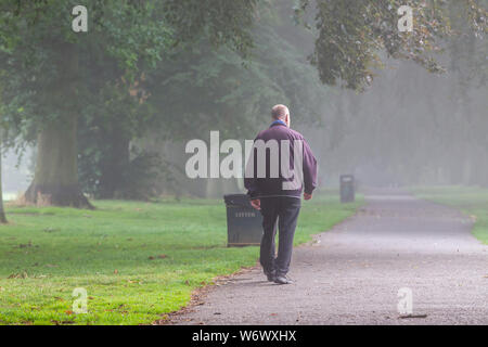 Northampton, Regno Unito. Il 3° agosto 2019. Meteo. Un uomo che cammina verso il viale di alberi di Abington Park nella nebbia di mattina presto con esso la cancellazione prima di 8am come la rosa di sole nel cielo di bruciarlo off. Credito: Keith J Smith./Alamy Live News Foto Stock