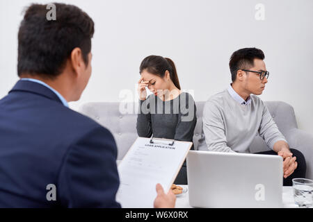 Non è colpa mia! Orinato giovane uomo che parla di psichiatra e gesticolando mentre sua moglie seduta vicino a lui e mantenendo le braccia incrociate Foto Stock