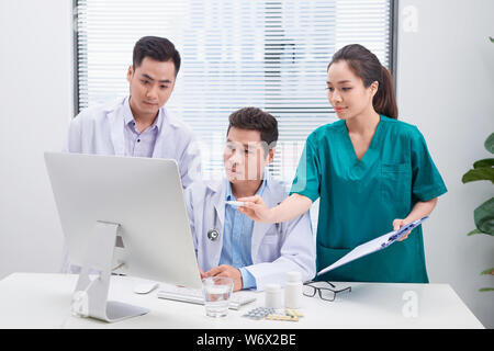 Tre medici a discutere dei file del paziente su office. Foto Stock