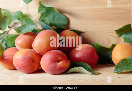 Albicocche con foglie su un sfondo di legno. Foto Stock