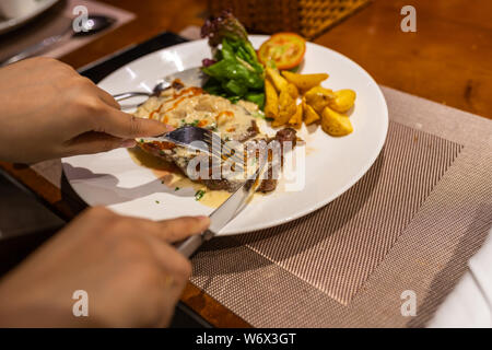 Mano umana il taglio di una deliziosa bistecca di controfiletto su piastra bianca Foto Stock